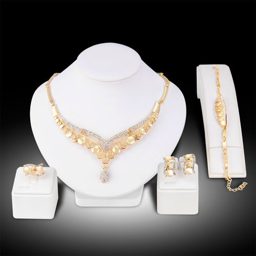 Gold jewelry set including necklace, bracelet, ring, and earrings on a white stand with a black background.