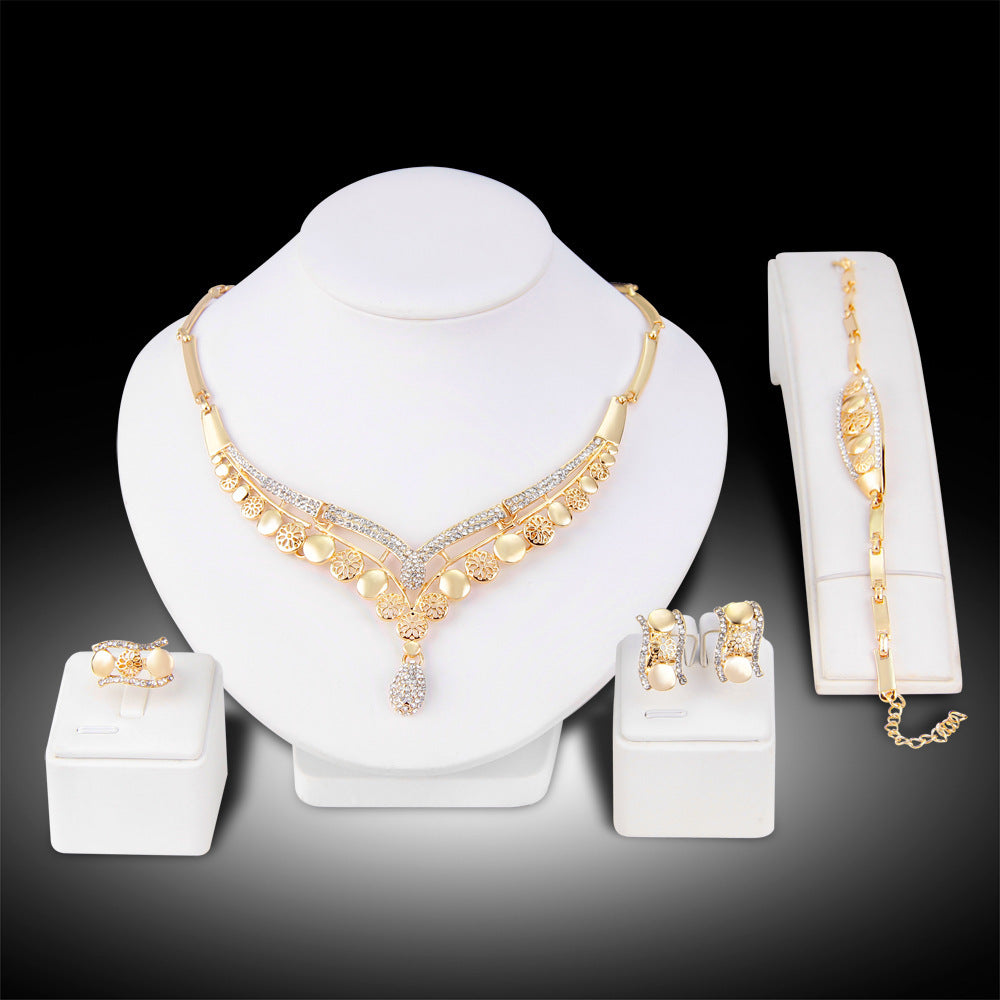 Gold jewelry set including necklace, bracelet, ring, and earrings on a white stand with a black background.